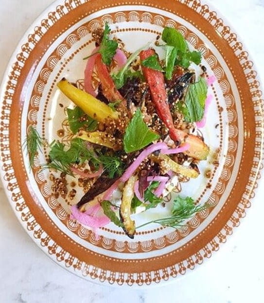 Roasted carrots with garnishes on a patterned plate on a marble kitchen countertop.